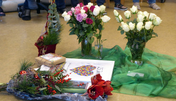 Auf einem grünen Tuch auf dem Boden stehen Blumen und Geschenke.