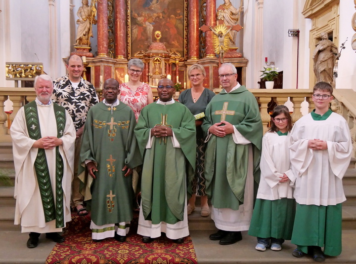 Das Bild zeigt eine Gruppe von Menschen, die auf Altarstufen in einer Kirche stehen. Sie schauen in die Kamera. Die Atmosphäre ist freundlich-fröhlich.