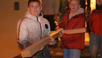 Zwei Kinder tragen ein Holzkreuz mit ihren Händen.
