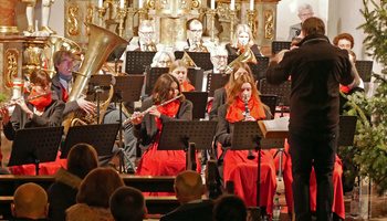 Blick vom Kirchenraum auf einen Teil der Musikkapelle. Der Dirigent steht mit dem Rücken zur Kamera.