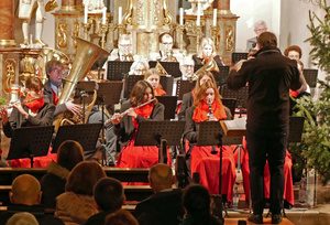 Blick vom Kirchenraum auf einen Teil der Musikkapelle. Der Dirigent steht mit dem Rücken zur Kamera.