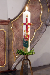 Eine Osterkerze steht auf einem Ständer in der Kirche. Sie brennt.