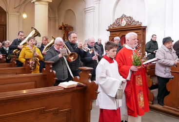 Der Pfarrer geht singend durch den Mittelgang der Kirche. Neben und hinter ihm sind Menschen mit Palmzweigen in den Händen.