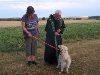 Pater Matthäus segnen einen kleinen Hund mit Weihwasser. Seine Herrin hat ihn an der Leine.
