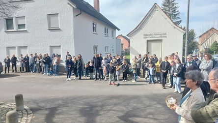 Um einen freien Platz in der Mitte stehen Menschen im Sonnenlicht. Sie halten teilweise Kerzen in ihren Händen.