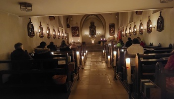 Man sieht die Kirche in Püssensheim mit Blickrichtung von hinten nach vorne, die Kirche ist dunkel und wird nur durch Kerzenschein erleuchtet