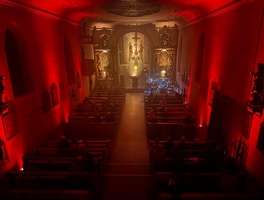 Blick von der Empore auf die Prosselsheimer Kirche, die mit roten Strahlern erleuchtet ist. Der Altarraum ist golden bestrahlt.