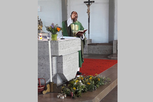 Der Pfarrer steht hinter dem Altar und hebt segnend die rechte Hand. Vor dem Altar liegen mehrerer Kräutersträuße.