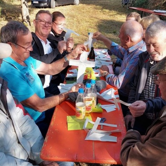 Menschen sitzen um einen Biertisch und schneiden aus weißem Papier Kreuze aus.